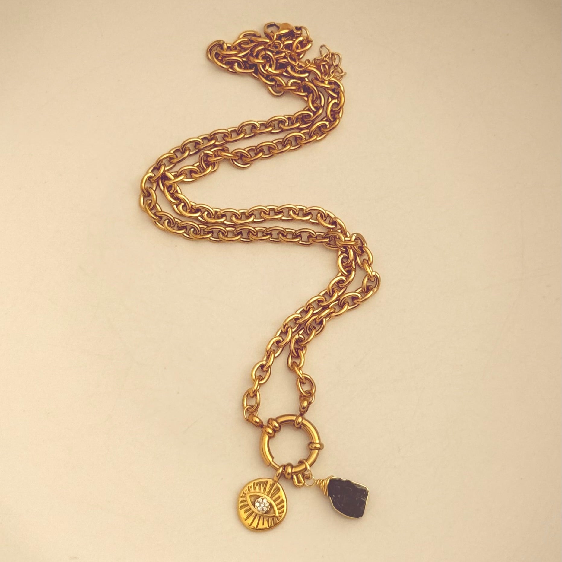 Gold chain necklace with a black stone pendant on a beige background
